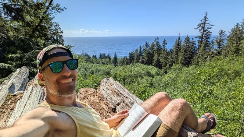 Justin reading on a log overlooking the ocean